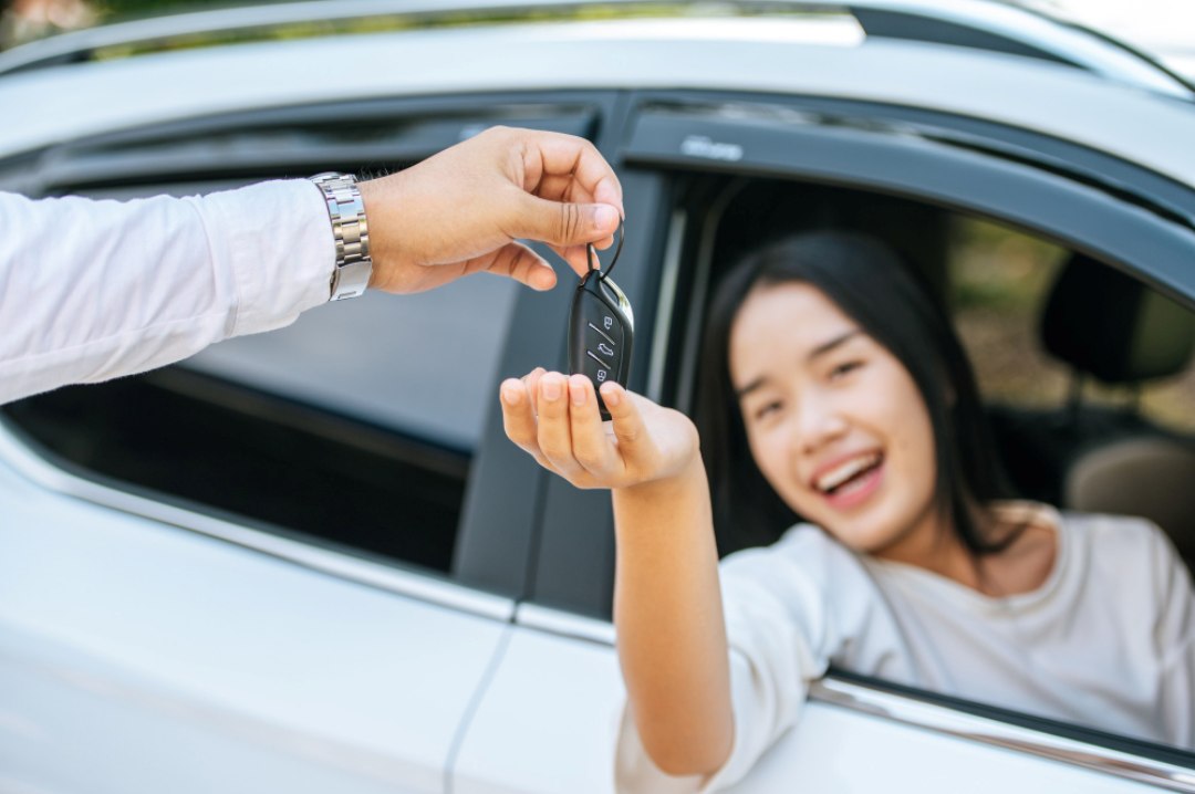 Seorang wanita menerima kunci kereta sewa dengan senyuman, melambangkan kemudahan dan keselamatan dengan insuran kereta sewa.